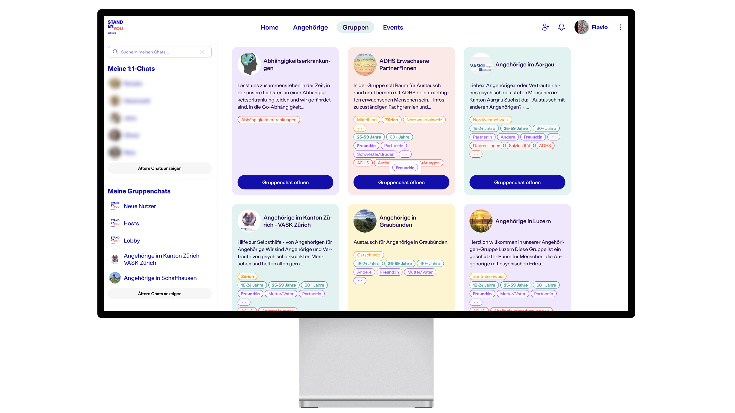 A computer monitor displays a volunteer platform’s social interface with colorful group cards, navigation tabs for Home, Angebote, Gruppen, and Events, and a sidebar showing chat and conversation options. A computer monitor displays a volunteer platform’s social interface with colorful group cards, navigation tabs for Home, Angebote, Gruppen, and Events, and a sidebar showing chat and conversation options.